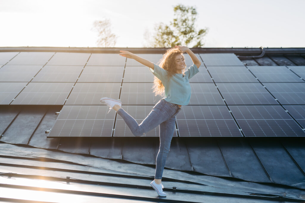 Frau tanzt auf Dach vor PV-Anlage